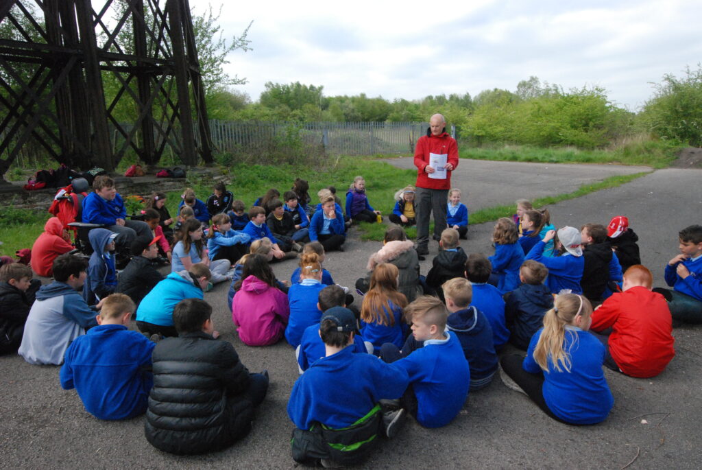 The images shows a teacher with a class of children who are sitting down under the viaduct. The teacher was recalling stories of the Zeppelin bombings in 1916