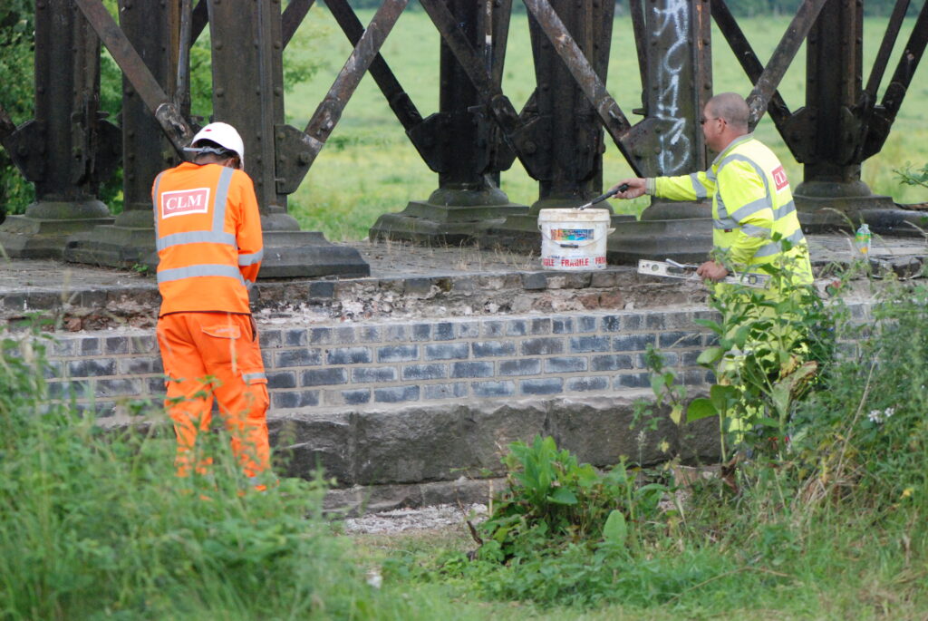 Workmen rebuild one of the crumbling brick pier bases using lime mortar