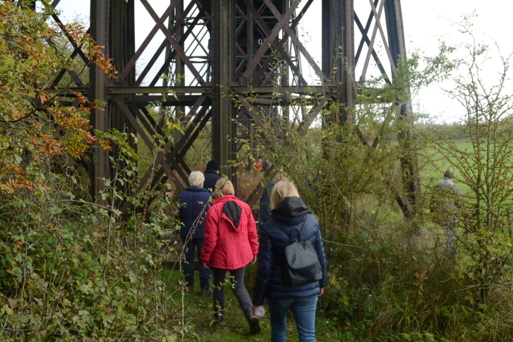 The image shows people walking under the viaduct through thick vegetation. It is possible to get up close to the structure and see how it was designed and built.
